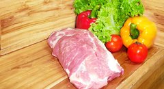 Schweinenacken vor einem hölzernen Hintergrund mit Gemüsedekoration