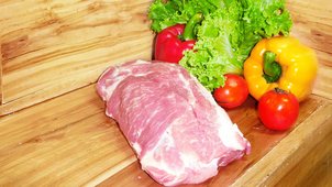 Schweinenacken vor einem hölzernen Hintergrund mit Gemüsedekoration