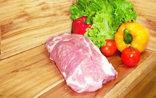Schweinenacken vor einem hölzernen Hintergrund mit Gemüsedekoration