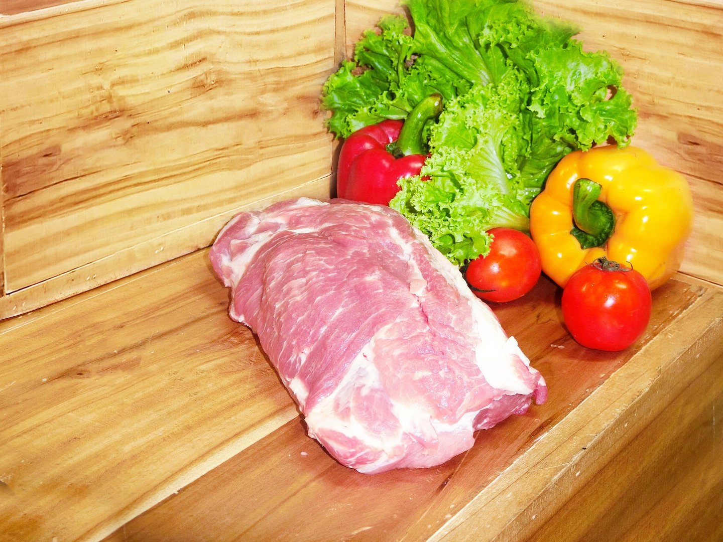 Schweinenacken vor einem hölzernen Hintergrund mit Gemüsedekoration