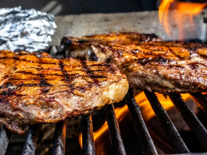 Zwei Rindersteaks mit Grillstreifen auf dem Rost, darunter lodernde Flammen